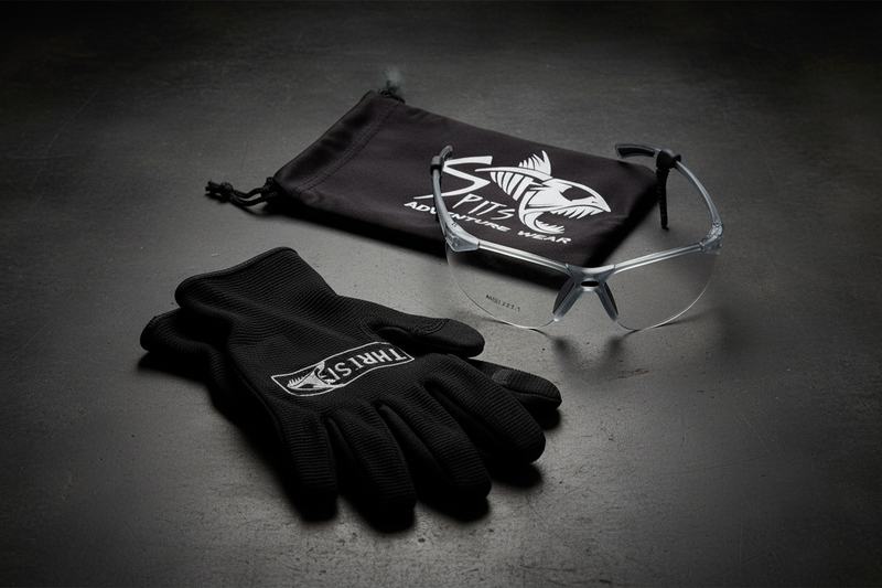 Spits Eyewear Thresher Z87.1 safety glasses lifestyle flat lay – translucent gray frame with clear lenses alongside black drawstring bag and work gloves