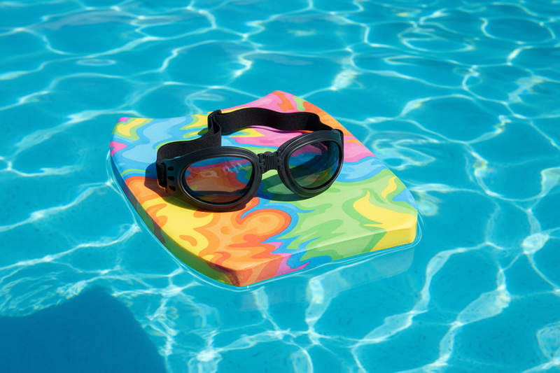 Adventure Jr folding goggles on a kids swim kickboard in a bright blue pool - Spits Eyewear